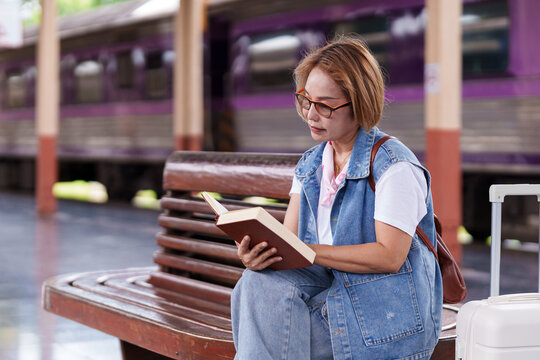 Asian older woman reads book while waiting train journey at railway station travel adventure tourism lifestyle vacation destination exploration
