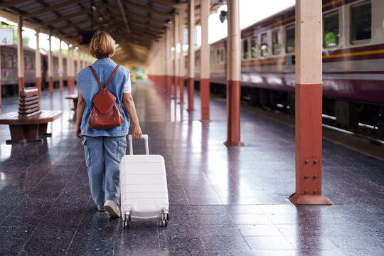 Asian older woman traveler journey train station platform pulling suitcase backpack vacation retirement adventure
