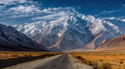 Majestic Snow-Capped Mountains Overlooking a Serene Road in Remote Wilderness under a Beautiful Blue Sky with Clouds in the Distance