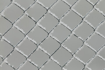 Fototapeta premium This image shows a closeup view of a chain link fence that is covered in a fresh layer of snow, creating a serene winter scene