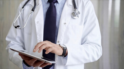 Doctor man wearing lab coat and stethoscope using tablet computer in hospital. Medicine and science