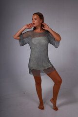 Beautiful barefoot young long haired woman in chainmail full length posing on grey background