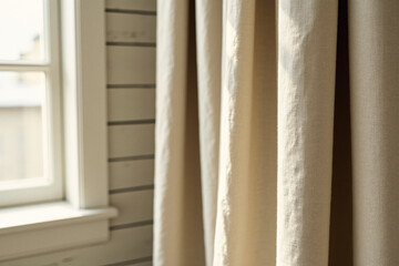 Sunlight streams through a window, illuminating textured linen curtains that hang beside paneled walls.