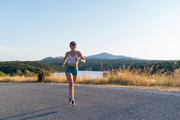 Young woman running on a country road near a lake at sunset