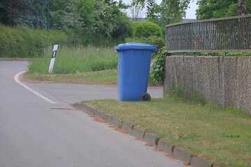 blue plastic bin with waste paper is at the curbside ready for collection