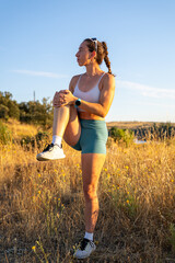 Young woman stretching legs in a meadow at sunset: exercising outdoors