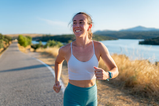 Young sporty woman running on a country road near a lake in summer