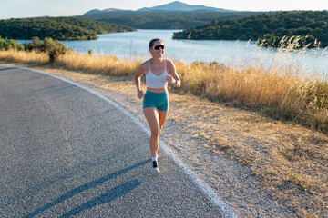 Young athlete running on a country road with a scenic mountain lake in the background during summer