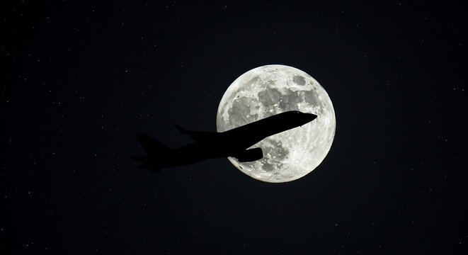 Commercial airplane silhouetted by the moon in a starry night sky