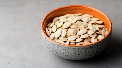 A bowl of raw pumpkin seeds on a textured surface, showcasing their natural color and shape.