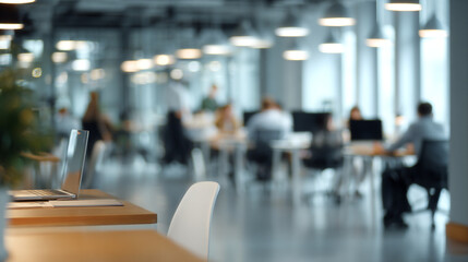 Fototapeta premium A blurred view of a modern office space with people working and a laptop in the foreground visible