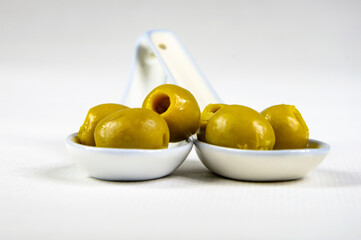 Olivas verdes sin hueso sobre cucharillas de porcelana blanca con fondo claro y difuminado