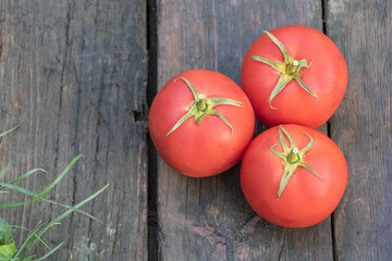 Three Fresh Ripe Tomatoes on Rustic Wooden Surface with Grass Nearby