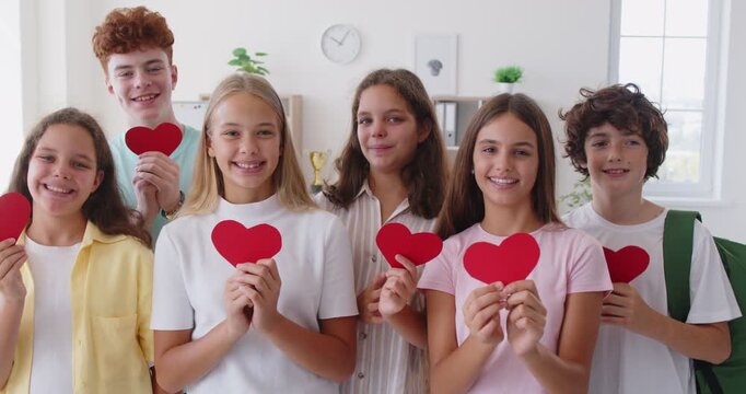Group of happy children who love school. Smiling kids friends boys and girls standing in the classroom holding heart shaped paper cards in their hands. Back to School concept - Powered by Adobe