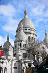 View of the main dome of Sacre Coeur basilica with cloudy blue sky and nearby rooftops in...