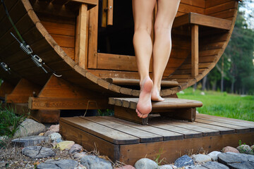 Close-up of female bare feet entering the outdoor wooden sauna from wooden stairs