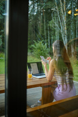 Back view at a woman working in the evening outdoors while sitting on the terrace of a log cabin