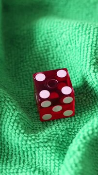 Un primer plano de un dado rojo en movimiento para juego en una tela de color verde como fondo. Video Vertical.