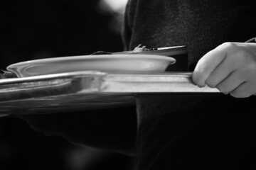 Black and white close-up of a server’s hand carrying a tray.