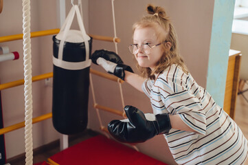 Empowered young girl with Down syndrome wearing boxing gloves, ready for a workout with a punching bag