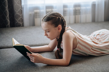 A girl comfortably lying on a sofa, engrossed in reading a book, depicting relaxation and quiet leisure