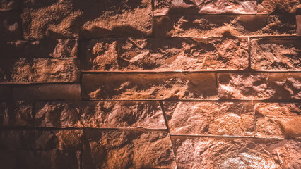 A textured wall made of reddish-brown stacked stones, lit by a warm light