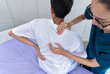 Young asian man patient undergoes chiropractic physical therapy under the supervision of a smiling...