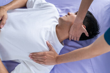 Young asian man patient undergoes chiropractic physical therapy under the supervision of a smiling...