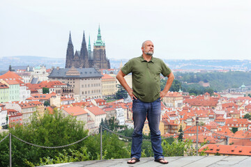 Traveler in green shirt admiring panoramic view of old Prague from hilltop viewpoint.