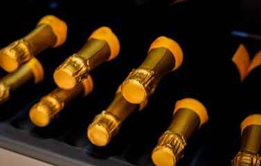 closeup stacks golden champagne bottles tops arranged in cold wine chiller shelf. on dark background. 
