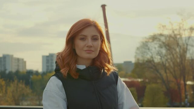 A redheaded young mother strolls through a park, enjoying the fresh air while caring for her baby in a stroller on a pleasant day with clear skies.
