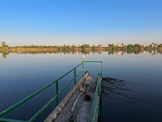 Panoramic landscape view across nile river to luxor west bank with water pipe and egret bird stood on railing