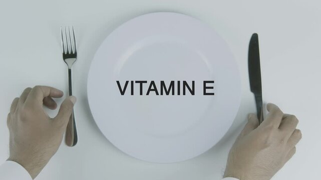 Vitamin E word on a plate with hands holding fork and knife on white background, symbolizing nutrition, healthy eating, dietary supplements, and wellness concept illustration