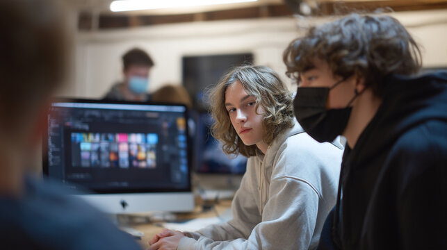 A group of young people wearing face masks working on computers in a brightly lit office space