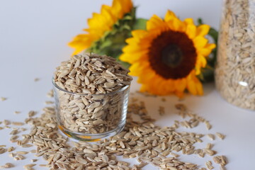 A glass brimming with sunflower seeds sits on a clean white surface, surrounded by scattered seed