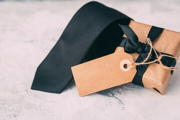 Close-up of a rolled up Black tie next to a wrapped gift box on a table for Father's Day