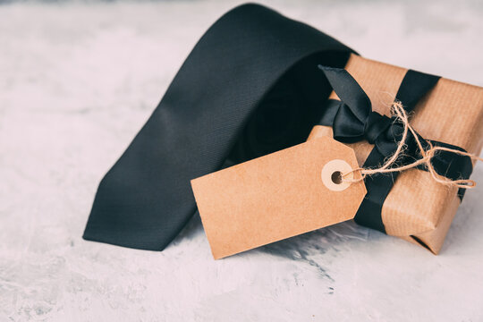 Close-up of a rolled up Black tie next to a wrapped gift box on a table for Father's Day