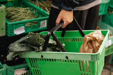 Close up of hand with a vegetables and greens in shopping basket on the local Farmers market....