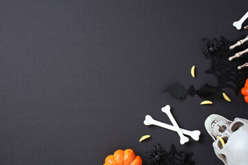 Festive Halloween flat lay on dark background featuring skull, crossed bones, pumpkins, bats,...