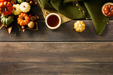 Rustic autumn flat lay with colorful pumpkins, pine cones, nuts, and acorns arranged in wooden leaf-shaped trays. A cozy tea cup, candle, and textured green cloth create a warm seasonal vibe