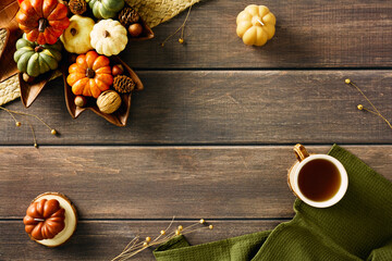 Rustic autumn flat lay with colorful pumpkins, pine cones, nuts, and acorns in leaf shaped tray. Cozy tea, candle, and textured cloth evoke seasonal warmth and festive charm.