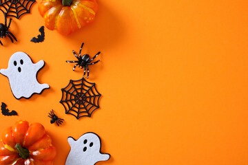 Halloween flat lay on vivid orange background featuring pumpkins, ghost cutouts, bats, spiders, and...