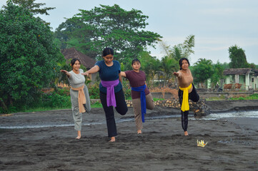 A group of girls in harmony performs yoga by standing on one leg and holding the other behind,...