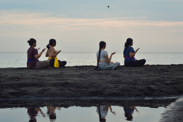 With eyes closed and palms facing up, the four girls sit quietly by the seaside as a small bird...