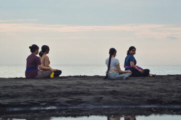 While sitting cross-legged on the beach, one of the girls provides subtle guidance as they prepare...