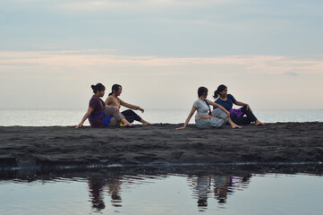 While seated cross-legged on the beach, the girls rotate their bodies to the right, one hand...