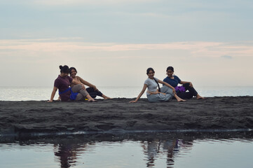 Facing the ocean, four girls sit cross-legged on the beach and twist rightward in unison, glancing...