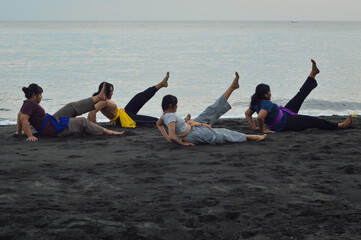 Sitting at the edge of the beach, the girls raise their left legs while leaning back slightly,...