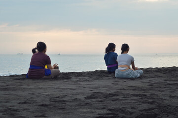 A peaceful morning with four teenage girls sitting cross-legged, viewed from behind, on the beach...