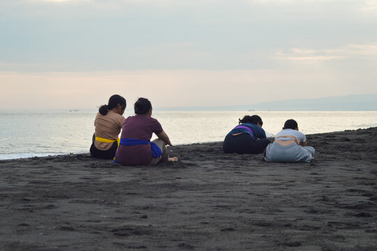 Moving into a deep stretch, the girls bend forward from a cross-legged pose with arms fully extended, embracing calmness and flexibility on the sand. - Powered by Adobe